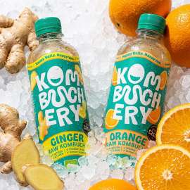 Je eine Flasche Kombuchery Ingwer und Orange auf Eis mit Ingwerknollen und Orangenscheiben