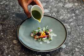 Gourmetk�che im Falkensteiner Balance Hotel Stegersbach: wundersch�n angrichtetes Lachfilet mit Bl�ten und Beeren aus dem Permagarten, ein gr�nes Kr�uter�l wird angegossen