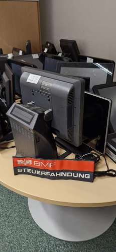 Auf einem Tisch mehrere beschlagnahmte PCs und Monitore mit einem Aufkleber 'BMF Steuerfahndung'