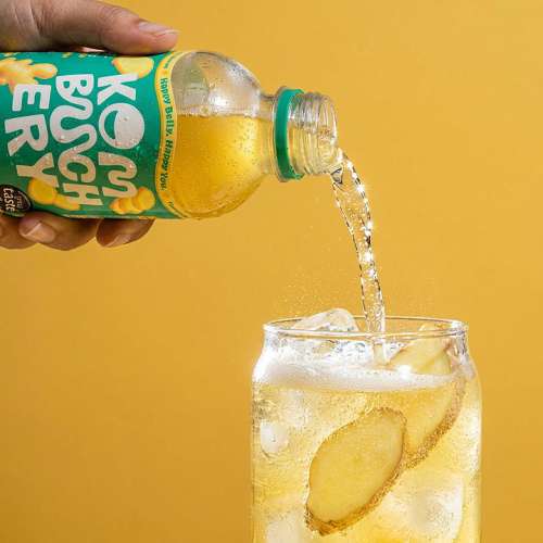 Kombuchery Orange wird aus der Flasche in ein Glas mit Eis und Zitrusscheiben eingeschenkt