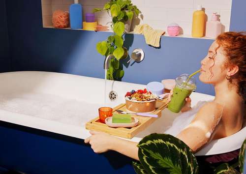 Eine Frau geniesst ein Bad in der Badewanne, in der Hand einen gr�nen Smoothie, vor Ihr auf einem Tablett ein gro�es Dessert